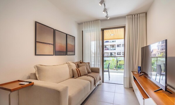 Un soggiorno moderno con divano, televisore e un balcone con vista sugli edifici.