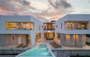 Una casa moderna de dos pisos con piscina, muros de piedra y varios balcones.