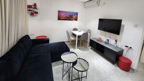 A modern living room with a black sectional sofa, a small round table, a TV, and a painting of a cityscape. - Charming two-bedroom apartment On The Sea Bat Yam (Bat Yam)
