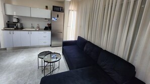 A modern living room with a dark sofa, a small coffee table, and a kitchen area with white cabinets and appliances. - Charming two-bedroom apartment On The Sea Bat Yam (Bat Yam)