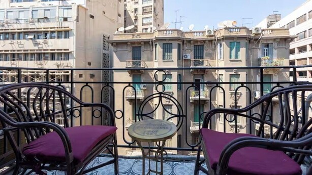 Ein Balkon mit Korbstühlen und einem kleinen Tisch, mit Blick auf eine Reihe von Gebäuden mit Balkonen.
