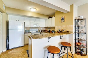 A kitchen with white cabinets, a granite countertop, a refrigerator, a microwave, a stove, and a wine rack. - 3 Mi to Dtwn Fort Myers: Condo w/ Pool Access (Fort Myers)