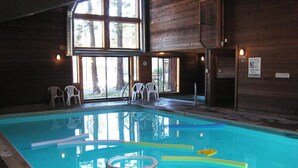Une piscine intérieure à l’eau claire, entourée de murs en bois et de grandes fenêtres.