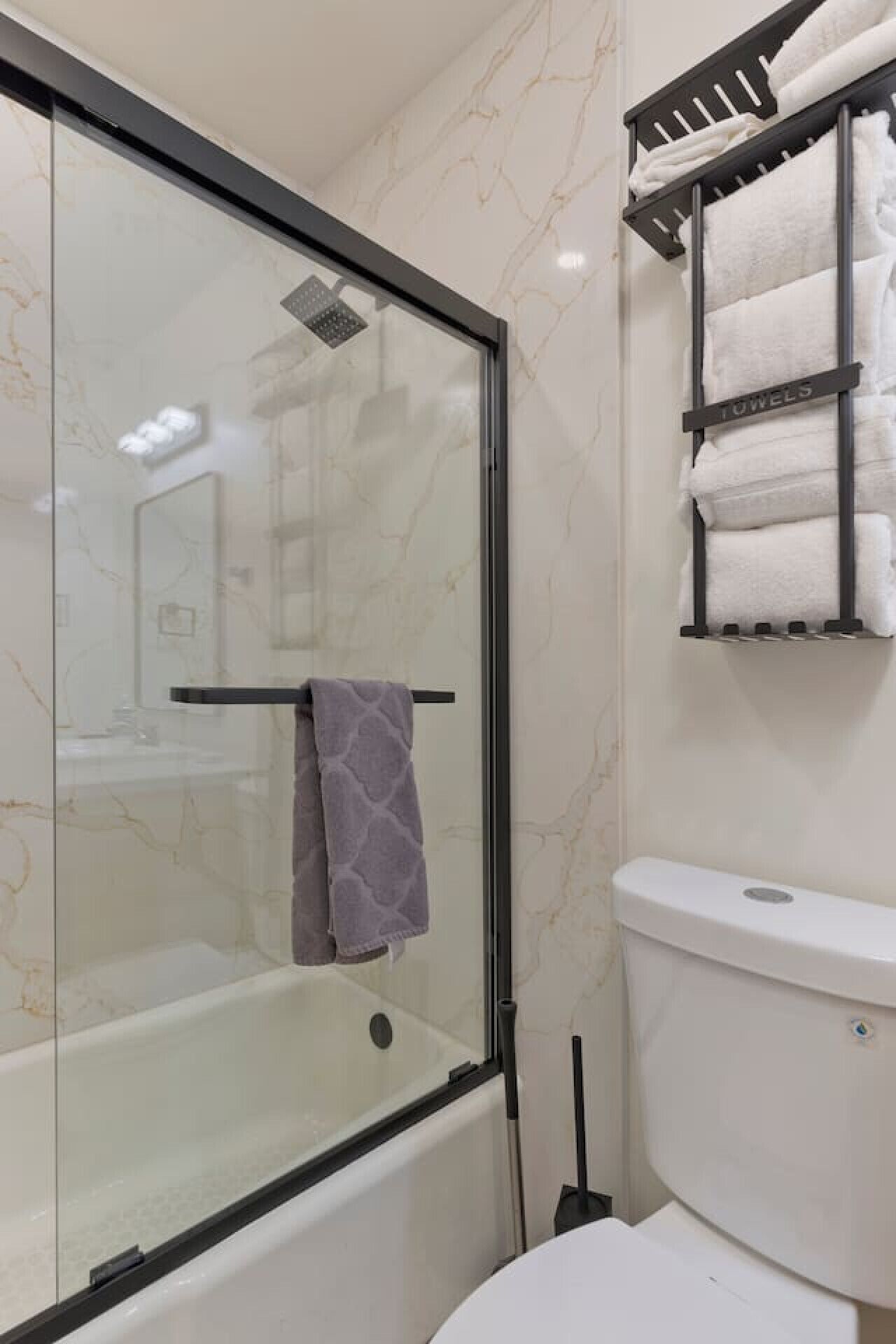 A bathroom with a glass-enclosed shower, a white toilet, and a towel rack with multiple towels.