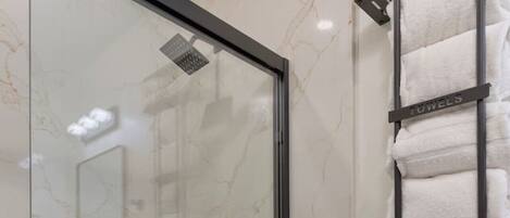 A bathroom with a glass-enclosed shower, a white toilet, and a towel rack with multiple towels.