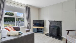 A living room with a sofa, a television on a stand, a fireplace, and a window with curtains. - The Wee House - Fáilte Ireland Quality Assured (Muff)