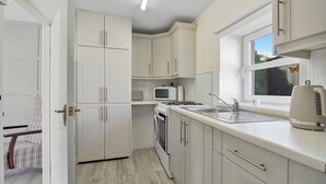 A compact kitchen with white cabinets, a microwave, a kettle, and a window. - The Wee House - Fáilte Ireland Quality Assured (Muff)