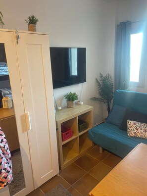A compact living space with a television mounted on a wall, a sofa with cushions, a small table, and a wardrobe with a mirror. - Sierra Nevada Study (Sierra Nevada)