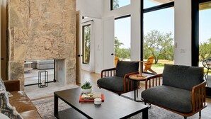 A modern living room with stone walls, large windows, and a view of the outdoors. - Ledgestone Ranch - Luxury Ranch - Pickleball - Bocce - Pool - Firepit (Wimberley)