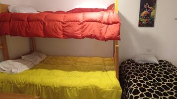 Un lit superposé avec un lit supérieur rouge et un lit inférieur jaune, un lit orné d’un motif girafe sur la droite, et un tableau accroché au mur.