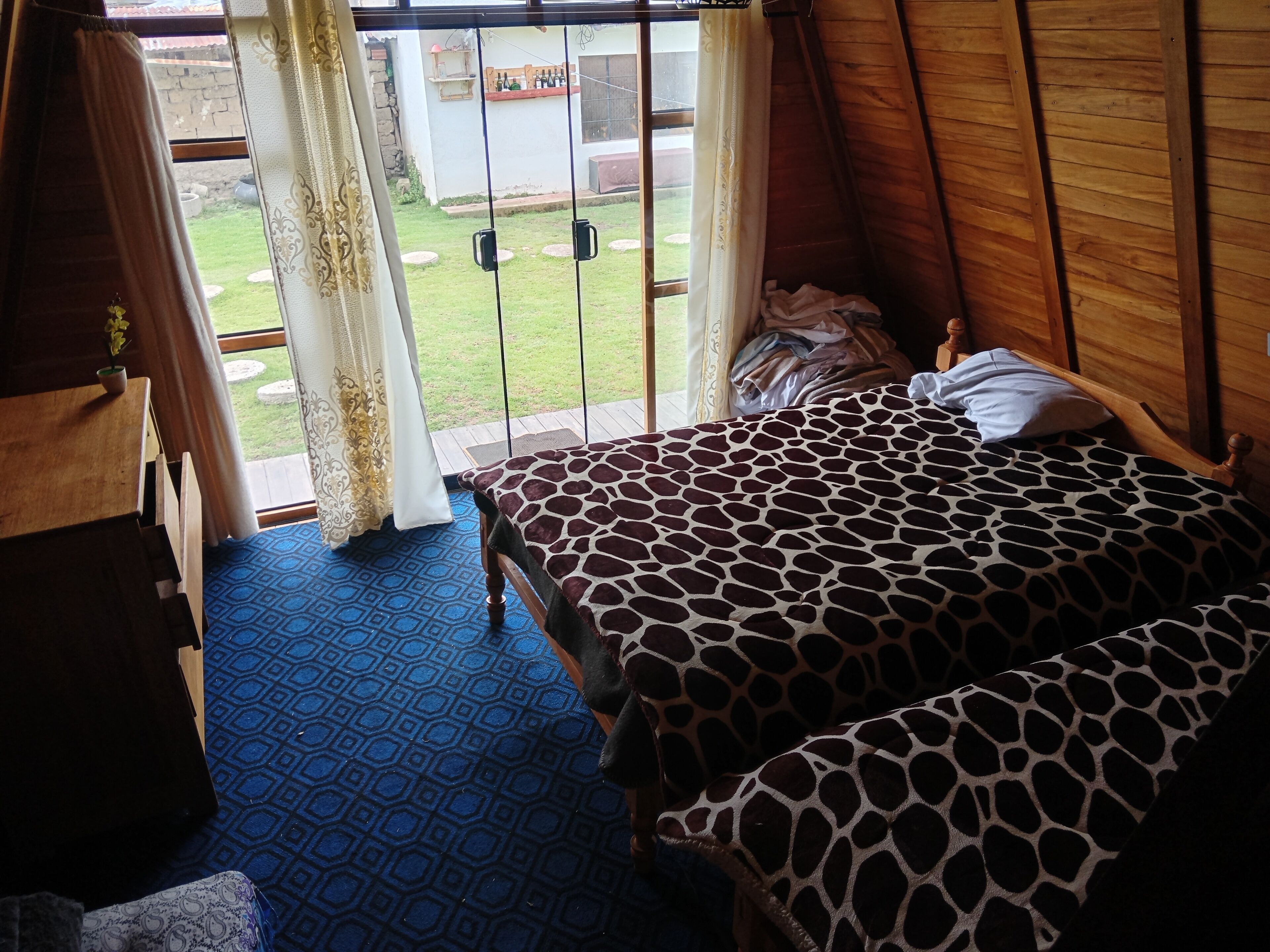 Una habitación con una cama, un armario de madera y vistas a un jardín por una ventana con cortinas.