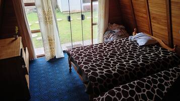 Una habitación con una cama, un armario de madera y vistas a un jardín por una ventana con cortinas.