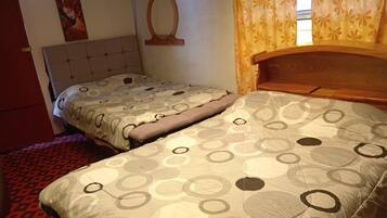 A room with two beds, a red door, a wall painting, a wooden headboard, and a window with curtains.