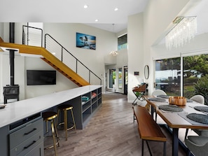 A modern kitchen with a wooden staircase, a built-in island, and a dining area with a view. - Ocean View Getaway (Manchester)