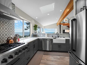 A modern kitchen with a large island, stainless steel appliances, and a view of the ocean. - Ocean View Getaway (Manchester)