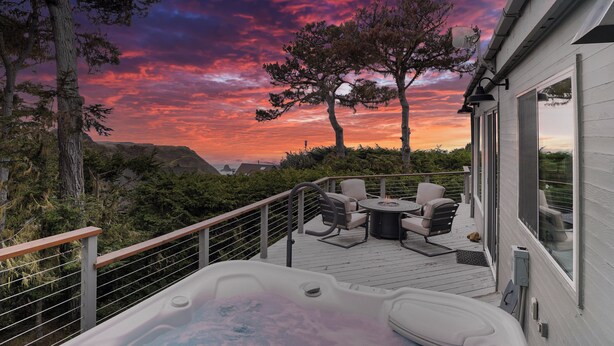 Ett bubbelbad på ett trädäck med utemöbler, med utsikt över ett vackert landskap med träd och en solnedgång.