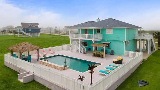 Una casa de dues plantes amb piscina, un porxo cobert i una tanca blanca.