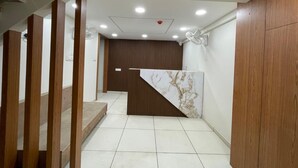 Una moderna zona de recepción con un mostrador de madera, un muro decorativo de mármol y suelo de baldosas.