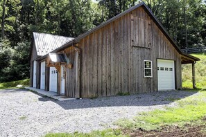 A wooden barn with two garage doors, a gravel driveway, and a metal roof.