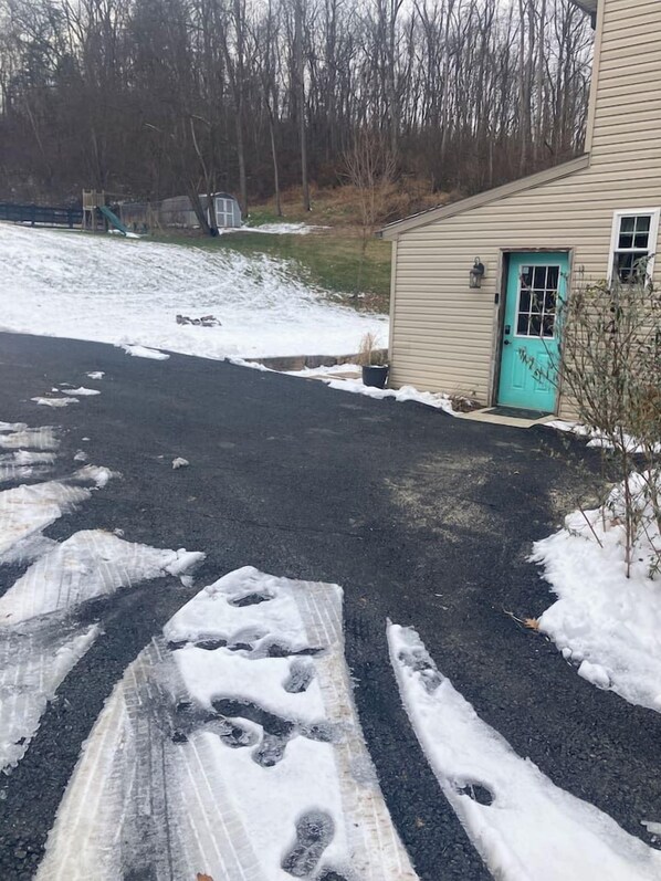 A residential driveway with snow patches and tire tracks, leading to a house with a turquoise door.