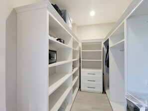 A narrow walk-in closet with white shelving and drawers, a small electronic device on one shelf, and a plastic bin on the right. - Speranza - Modern oceanview living in Hope Estate (Hope Estate)
