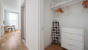 En gang med trægulv, et skrivebord med stole, en radiator og en tørrestativ med tøj.