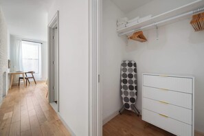 Ein Flur mit Holzboden, einem Schreibtisch mit Stühlen, einem Heizkörper und einem Wäscheständer mit Kleidung.