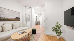 En moderne stue med sofa, sofabord, en potteplante og et fjernsyn ophængt på væggen.
