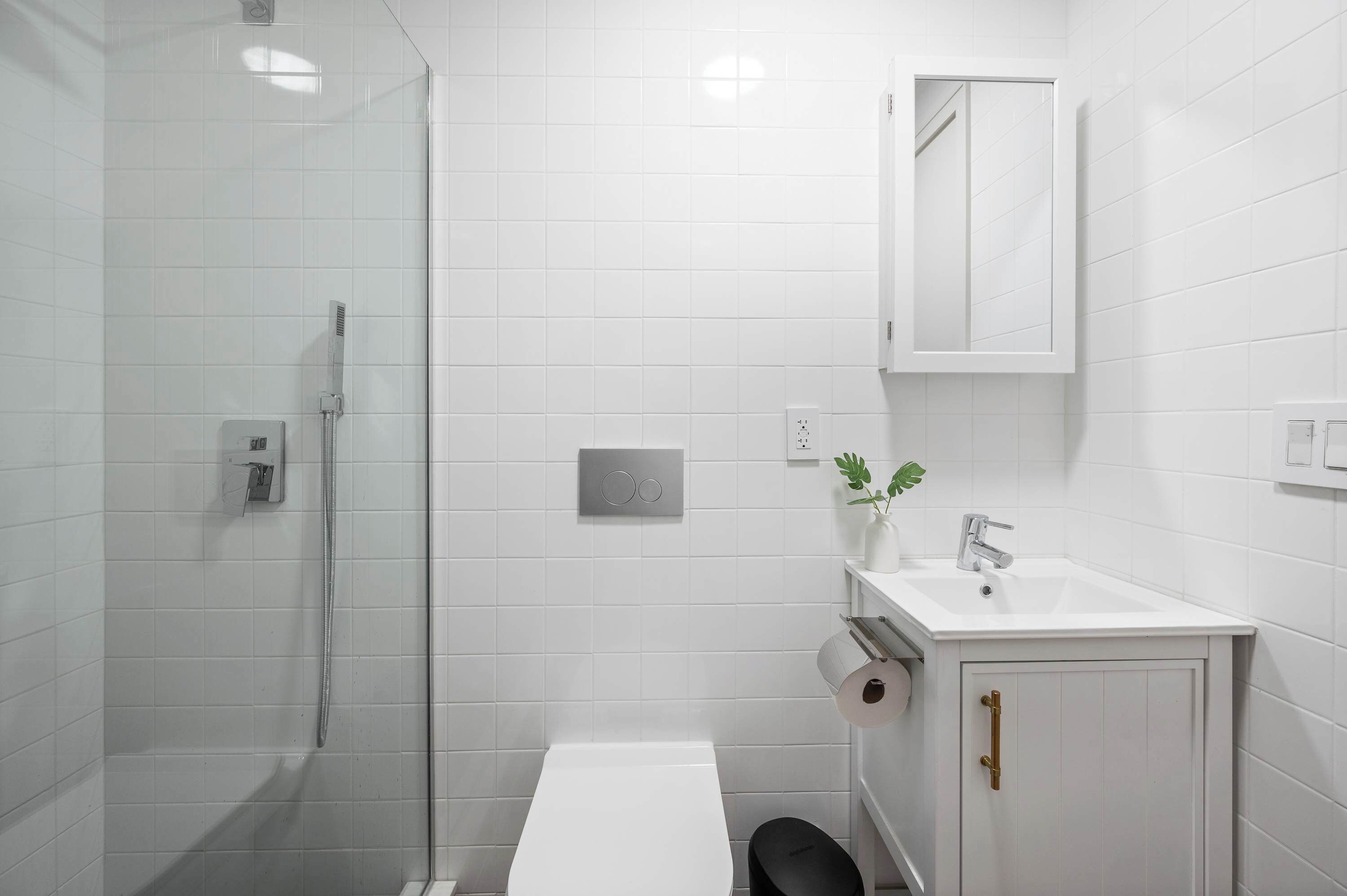 A modern bathroom with a glass shower enclosure, a white sink with a mirror above it, and a toilet.