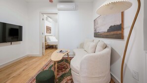 En moderne stue med et fladskærms-tv, en sofa, et lille bord og en gulvlampe.