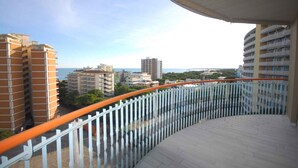 A balcony with a curved railing overlooking a cityscape with buildings and a distant view of the sea. - Holiday apartment mit Pool und Balkon (Lignano Sabbiadoro)