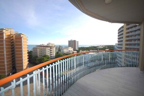 Ein Balkon mit geschwungener Brüstung, der auf die Stadtmitte mit Gebäuden und eine ferne Meerblick blickt.