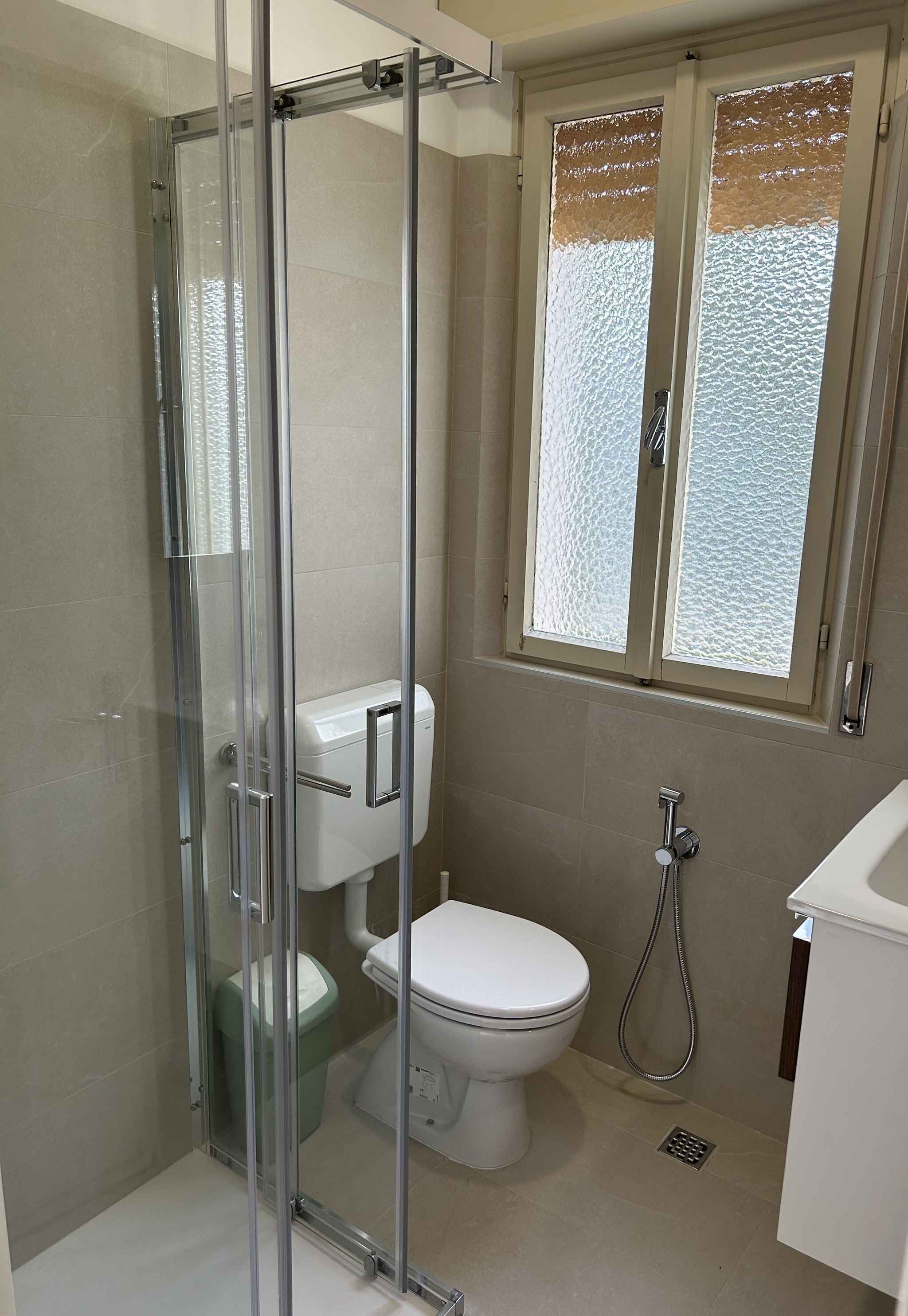 Un baño con ducha envuelta en vidrio, inodoro y ventana con vidrio esmerilado.