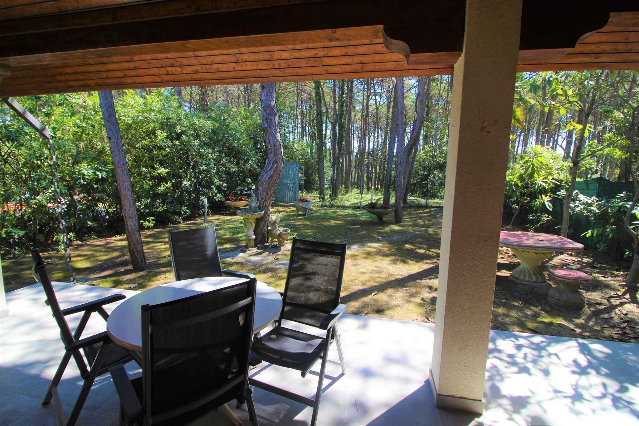 Un patio couvert, agrémenté d’une table et de chaises, entouré d’une zone boisée.
