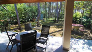 En overdækket terrasse med et bord og stole, omgivet af skov.