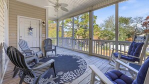 Eine überdachte Veranda mit zwei Adirondack-Stühlen, einem Deckenventilator und Blick auf Bäume und einen See.