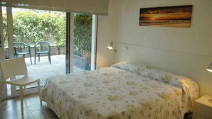 Ein Schlafzimmer mit Bett, Stuhl, Schreibtisch und einem Fenster mit Blick auf Grünflächen.