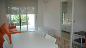 Ein Zimmer mit einem weißen Tisch, einem orangefarbenen Sofa und einem Bett im Hintergrund.