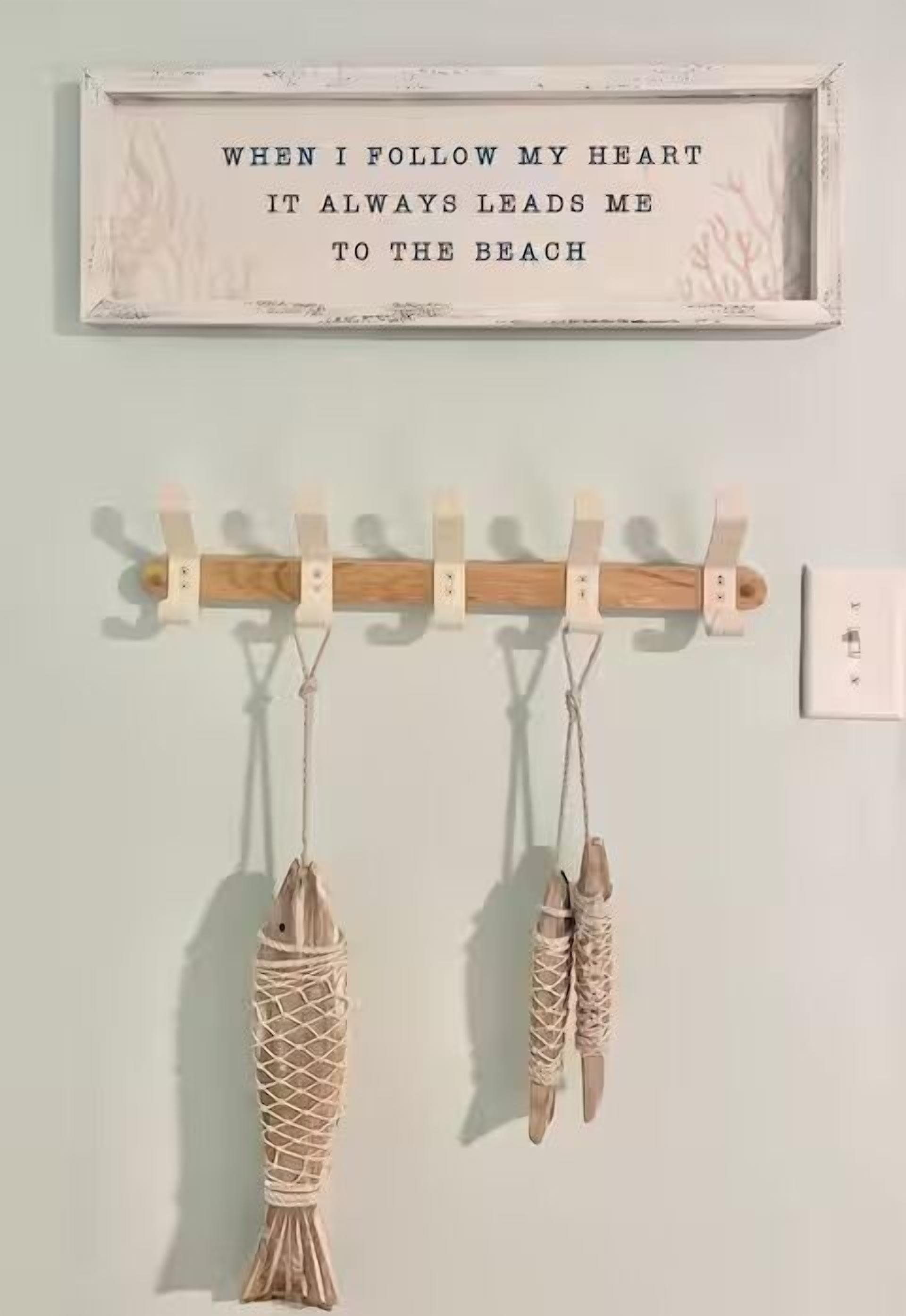 A wall with a framed quote and two fish-shaped decorations hanging on a wooden rack.