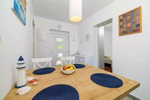 A dining area with a wooden table, blue placemats, a bowl of fruit, and a lighthouse decoration. - Holiday apartment with air conditioning and balcony (Selce)