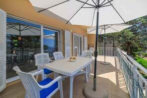 Eine Terrasse im Freien mit einem weißen Tisch und Stühlen, einem runden Tisch mit Obst und einem großen Sonnenschirm.