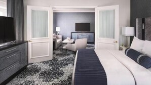 Une chambre d’hôtel avec un grand lit, une télévision, un bureau avec une chaise et une petite table avec une lampe.