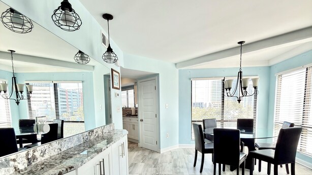 A modern kitchen with white cabinets, a granite countertop, and a dining area with a table and chairs. - 3BR/3BA Relax, Rewind, Enjoy, Oceanview & Coastal Breeze (Myrtle Beach)