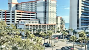 A modern hotel with multiple floors, a parking lot, and a view of the ocean. - 3BR/3BA Relax, Rewind, Enjoy, Oceanview & Coastal Breeze (Myrtle Beach)