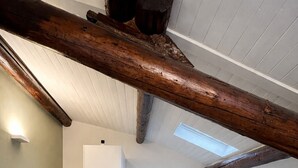 Un interior modern amb una separació de vidre, un sofà blanc i bigues de fusta a la vista.