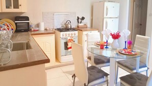 A compact kitchen with a gas stove, oven, and a refrigerator. There is a dining table with chairs and a glass top.