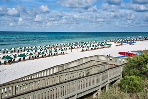 Ein Strand mit Reihen von Sonnenschirmen und Liegestühlen, einer Holzpromenade und Blick auf den Ozean.