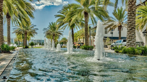 Une fontaine d’eau, des palmiers et un bâtiment en arrière-plan.