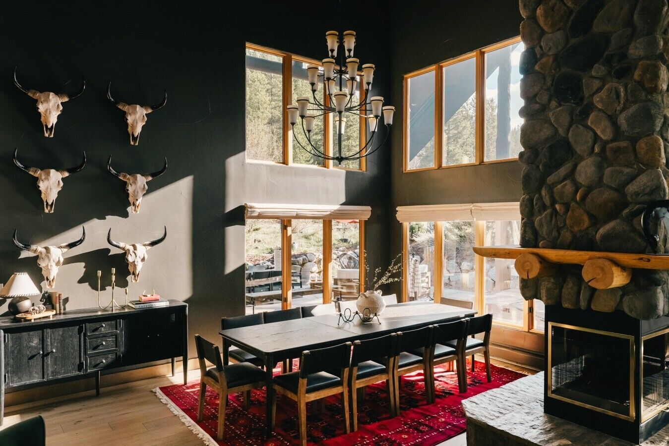 A dining area with a table, chairs, a chandelier, and a stone fireplace.