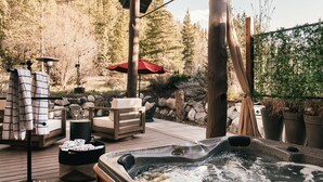 Ein Whirlpool auf einer Holzterrasse mit Gartenmöbeln, einem roten Sonnenschirm und Wald im Hintergrund.